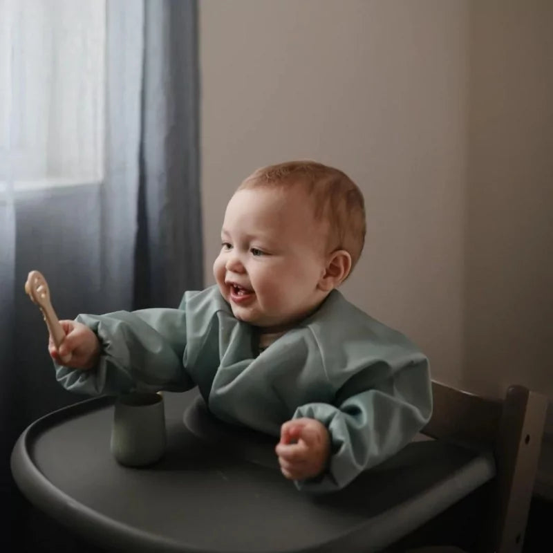 Bébé souriant en chaise haute tenant une cuillère en silicone