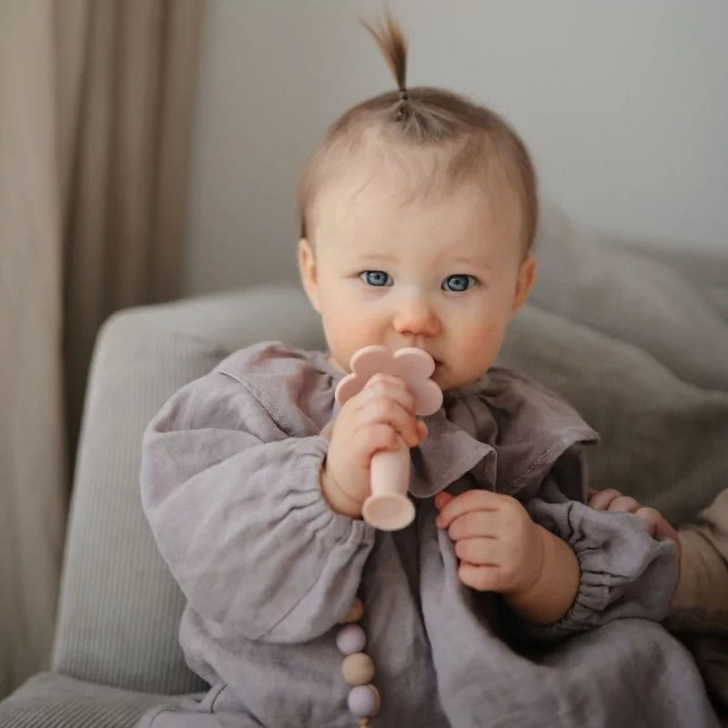 Bébé fille tenant une brosse à dent de dentition en silicone rose avec perles en bois
